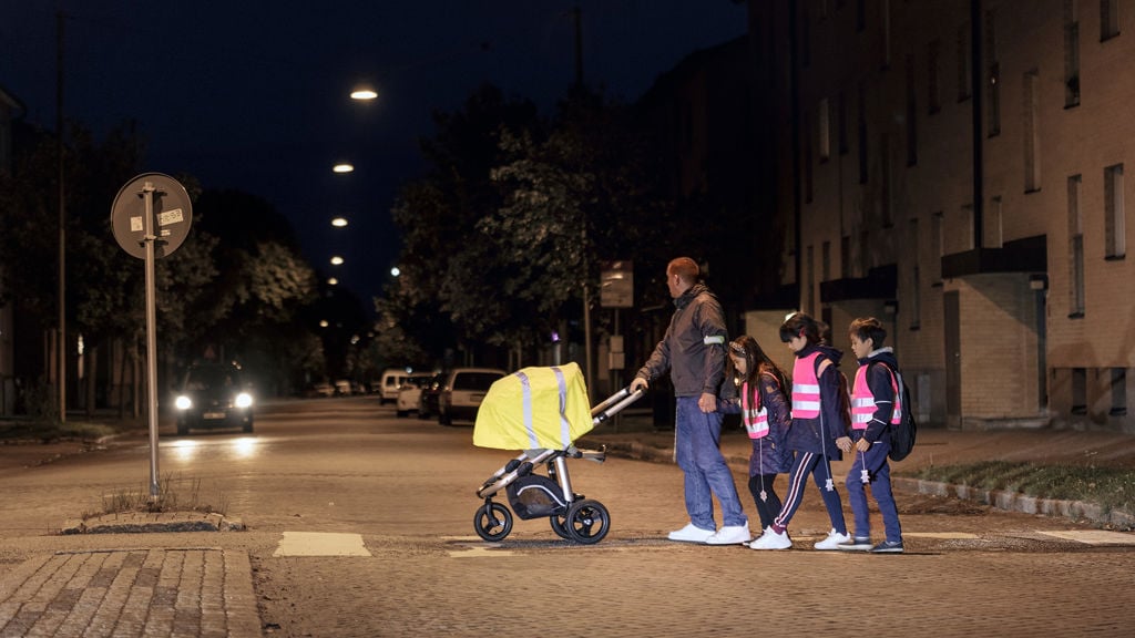 Pappa med barnvagn och tre barn går över ett övergångsställe på kvällen