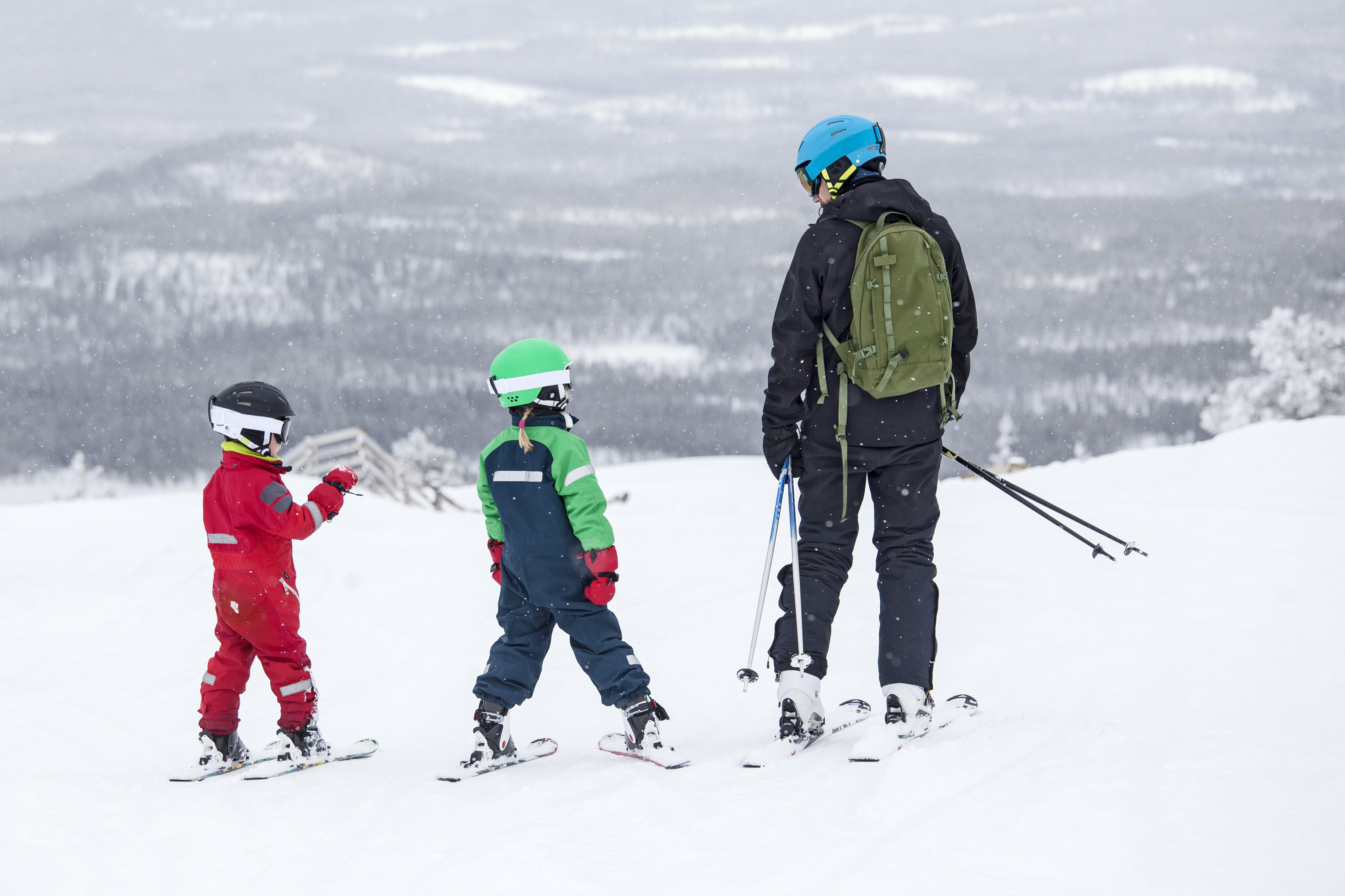 En vuxen och två barn i skidkläder och hjälm i skidbacke