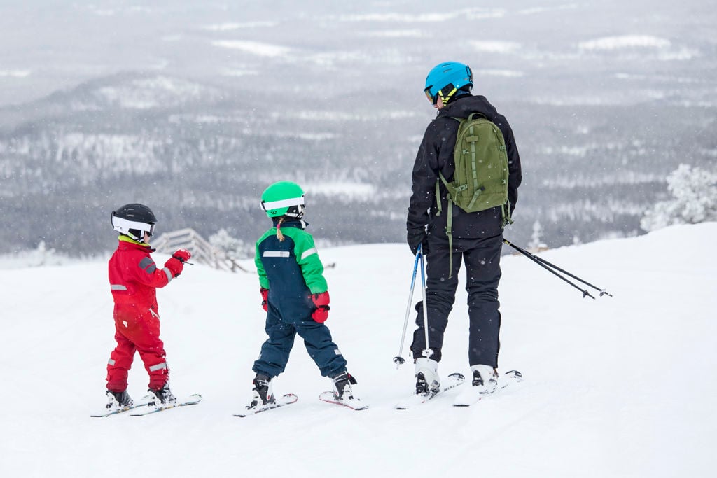 En vuxen och två barn i skidkläder och hjälm i skidbacke
