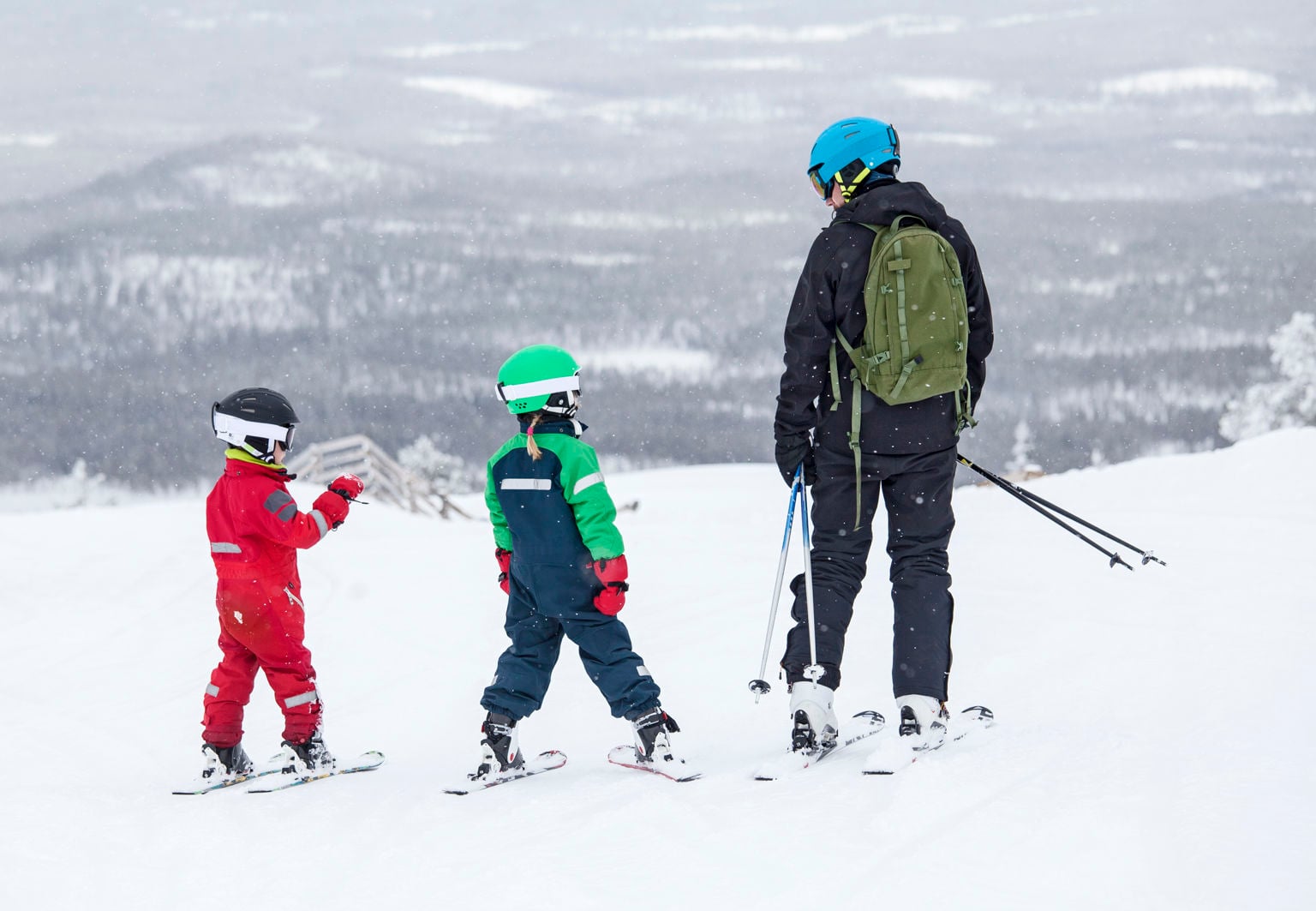 En vuxen och två barn i skidkläder och hjälm i skidbacke