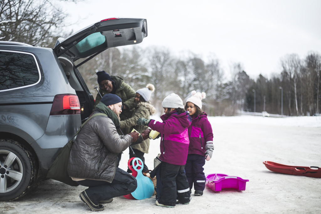Familj med tre barn packar ur pulkor och stjärtlappar bilen