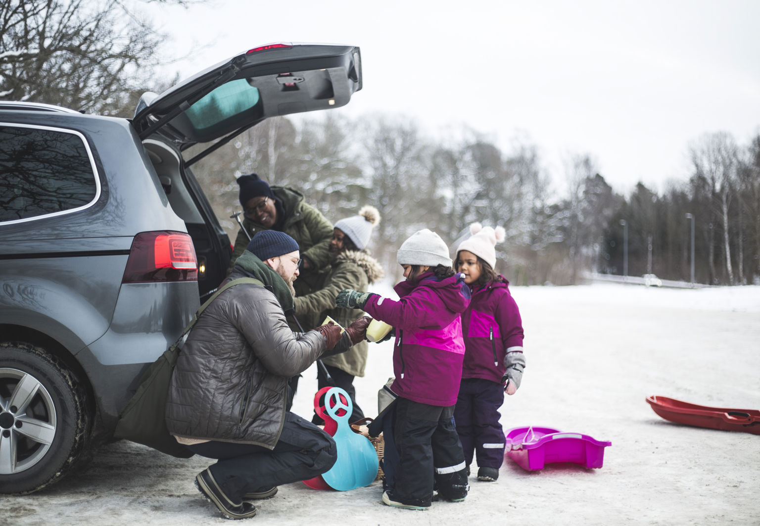 Familj med tre barn packar ur pulkor och stjärtlappar bilen