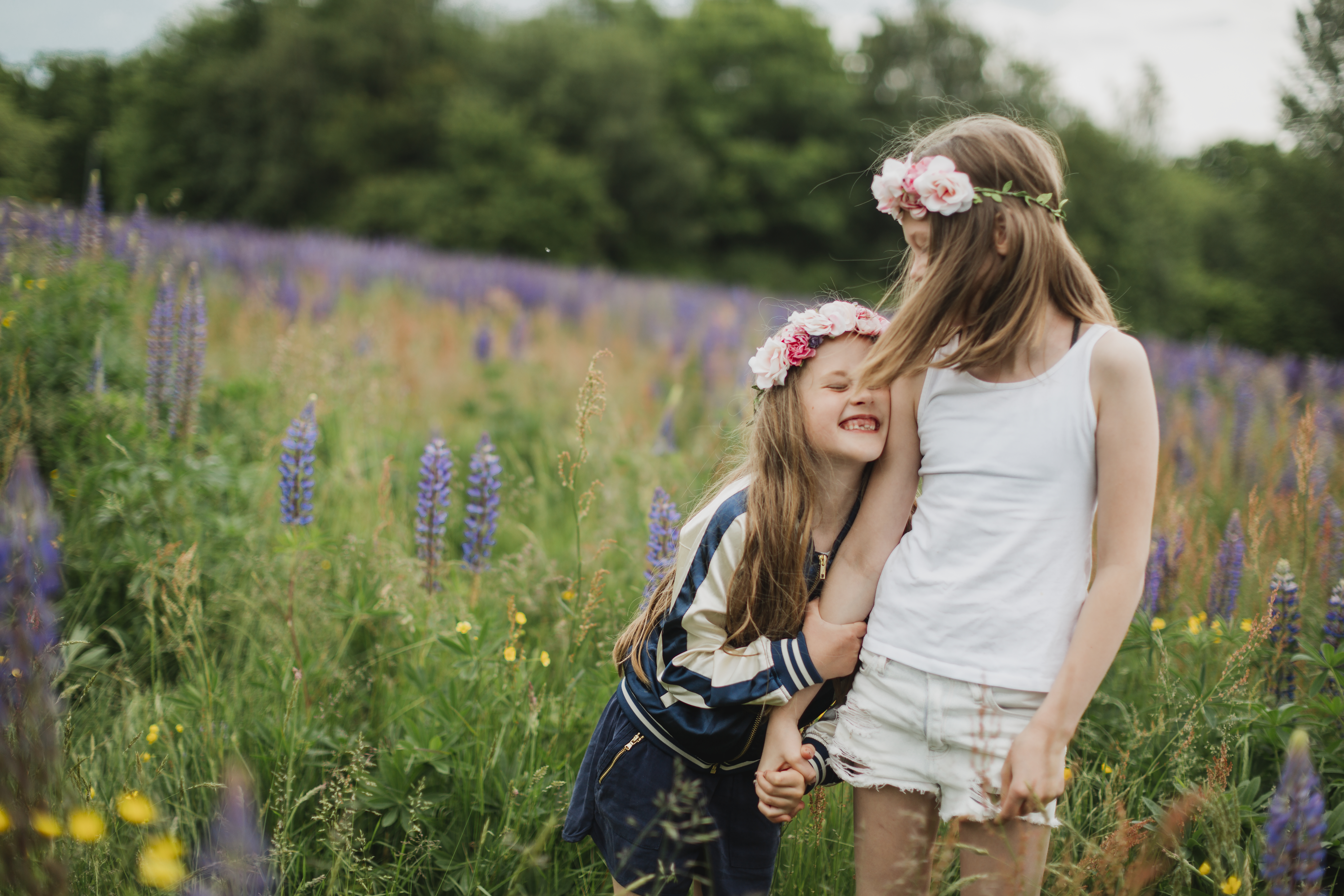 Två flickor med blomsterkrans i håret går hand i hand på en äng