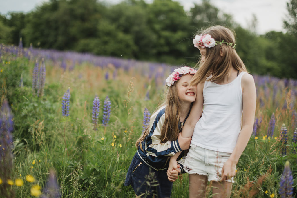 Två flickor med blomsterkrans i håret går hand i hand på en äng