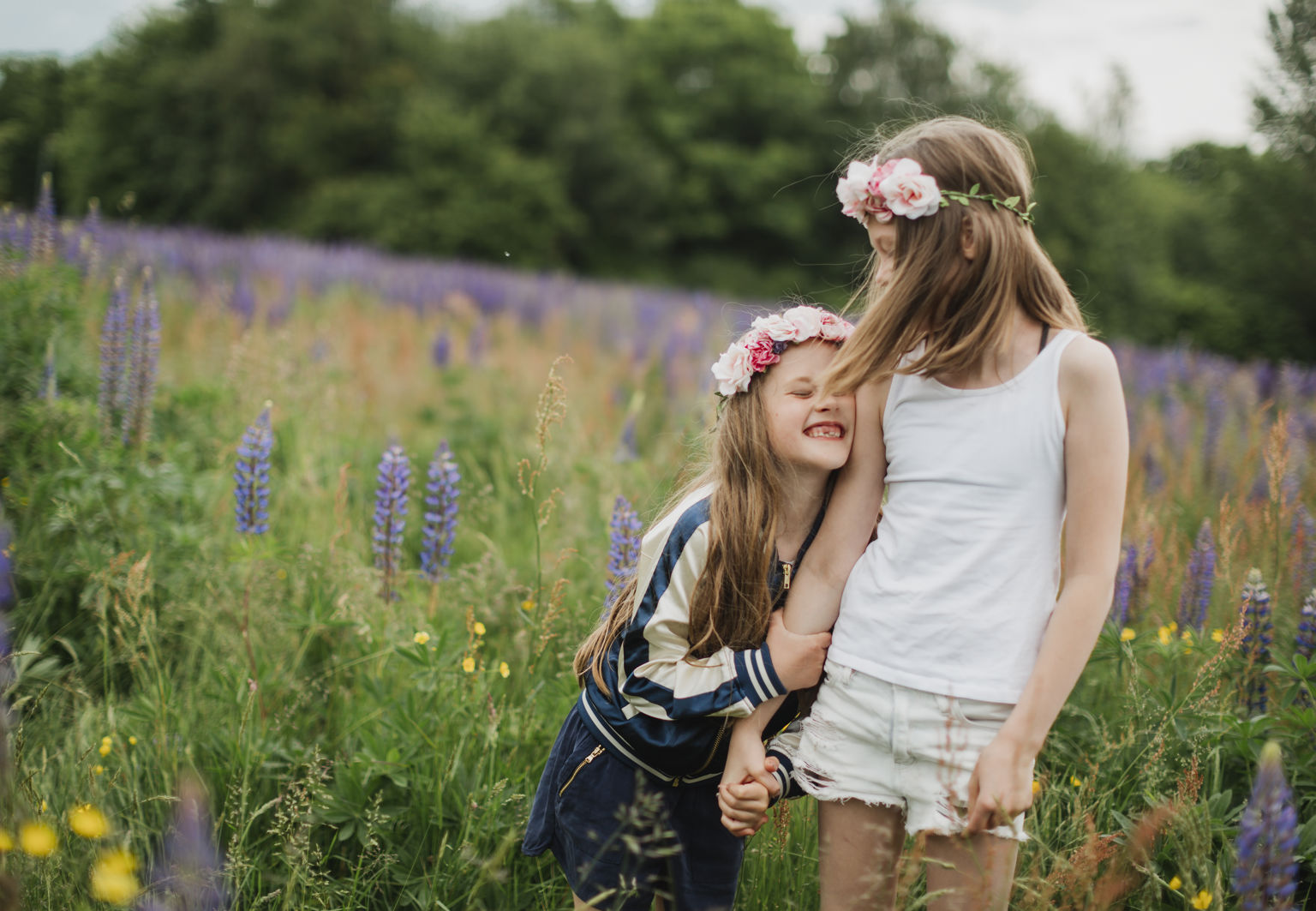 Två flickor med blomsterkrans i håret går hand i hand på en äng