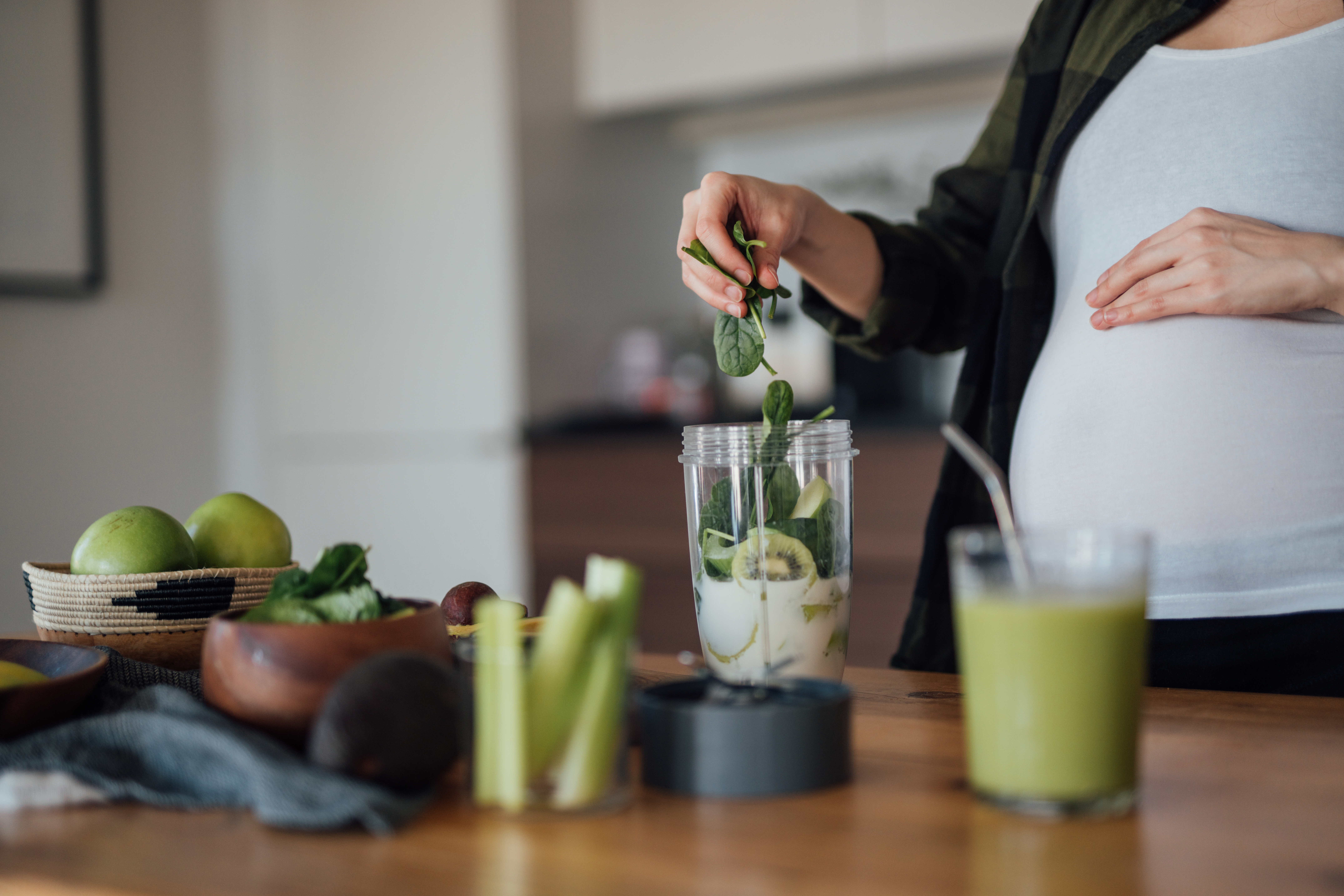 Gravid kvinna gör en smoothie med grönsaker och frukt
