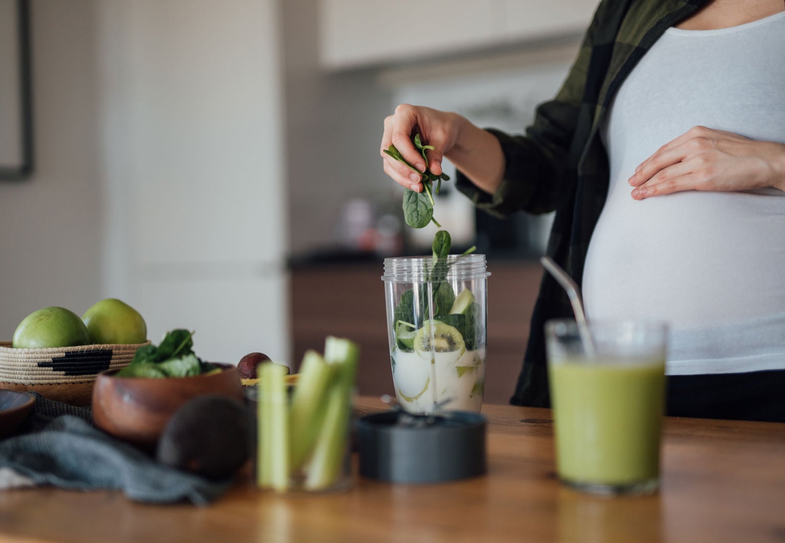 Gravid kvinna gör en smoothie med grönsaker och frukt