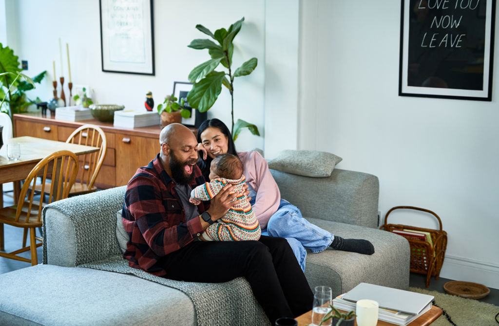 En pappa och mamma busar och pratar med barnet i en vardagsrumssoffa