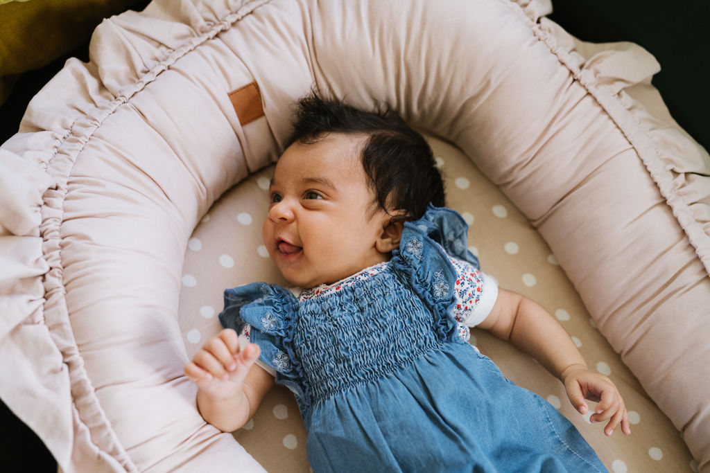Vaken och glad bebis ligger i ett babynest med klänning