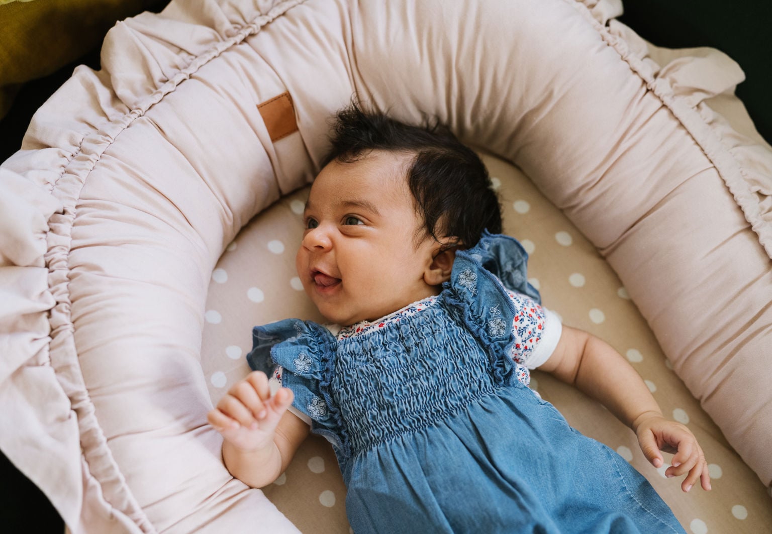 Vaken och glad bebis ligger i ett babynest med klänning