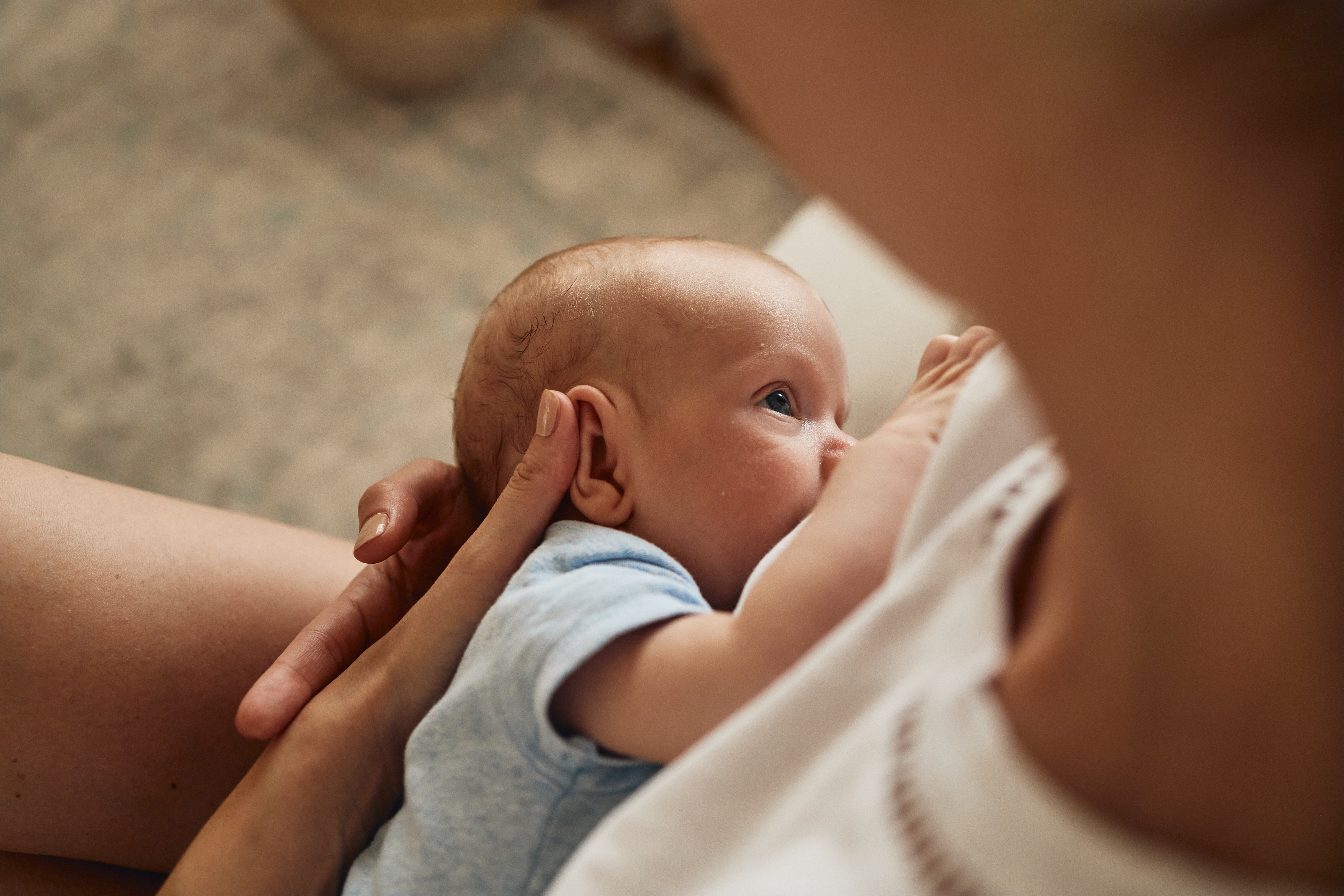 Vaken bebis ligger i sin mammas famn och ammar