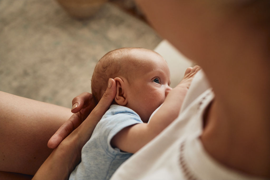 Vaken bebis ligger i sin mammas famn och ammar