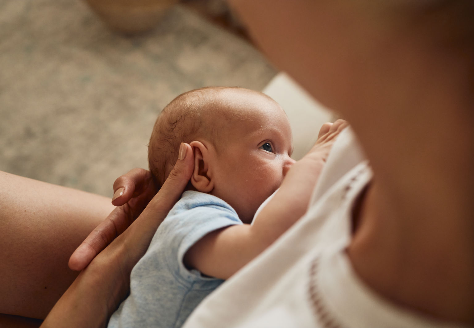 Vaken bebis ligger i sin mammas famn och ammar