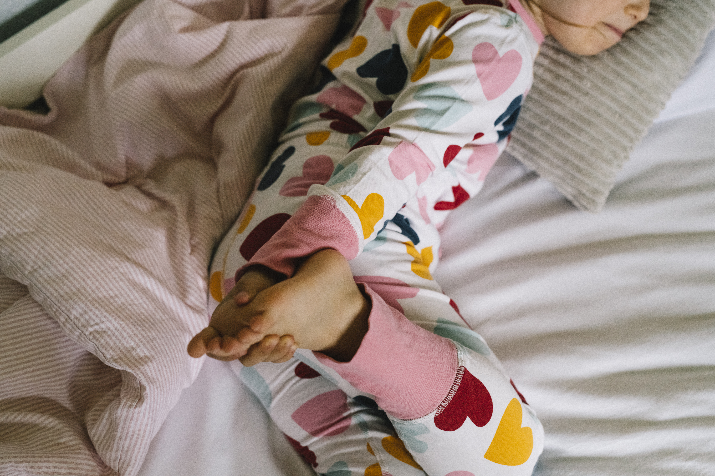 Barn klädd i pyjamas ligger i sin säng och håller i sin fot