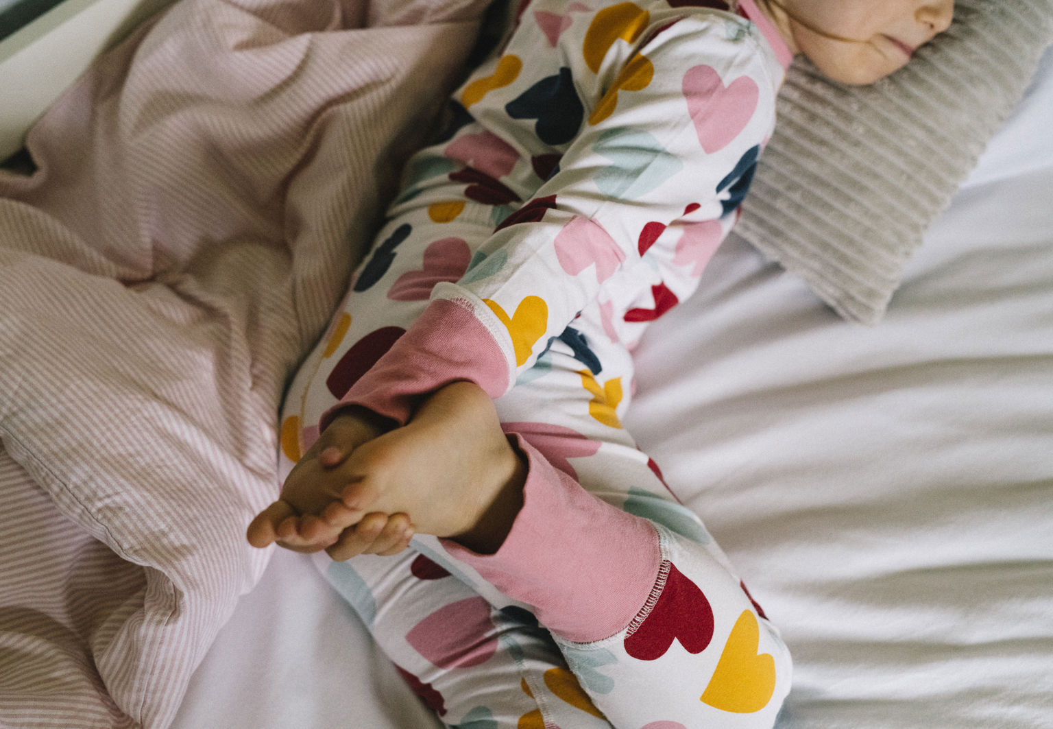 Barn klädd i pyjamas ligger i sin säng och håller i sin fot