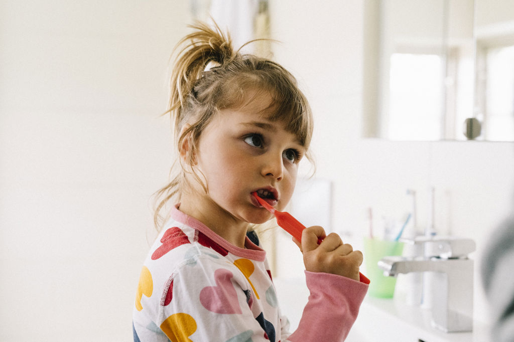 Flicka med pyjamas borstar tänderna i badrummet