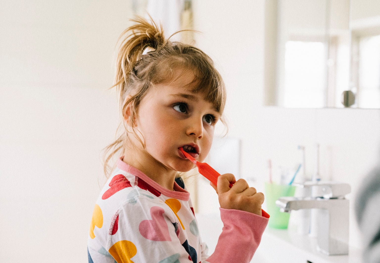 Flicka med pyjamas borstar tänderna i badrummet