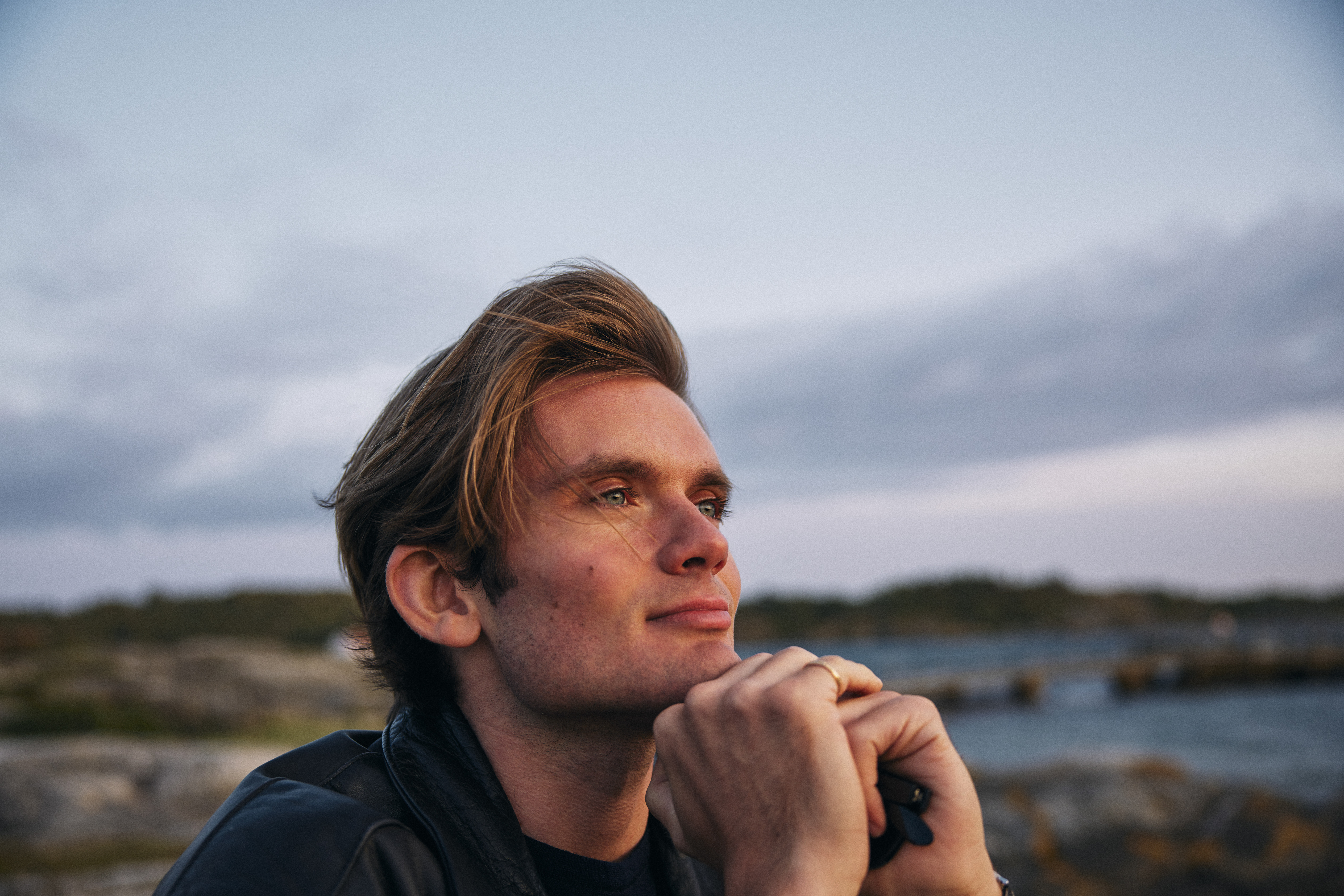 Fridfull bild på en man som sitter och småler utomhus vid vattnet