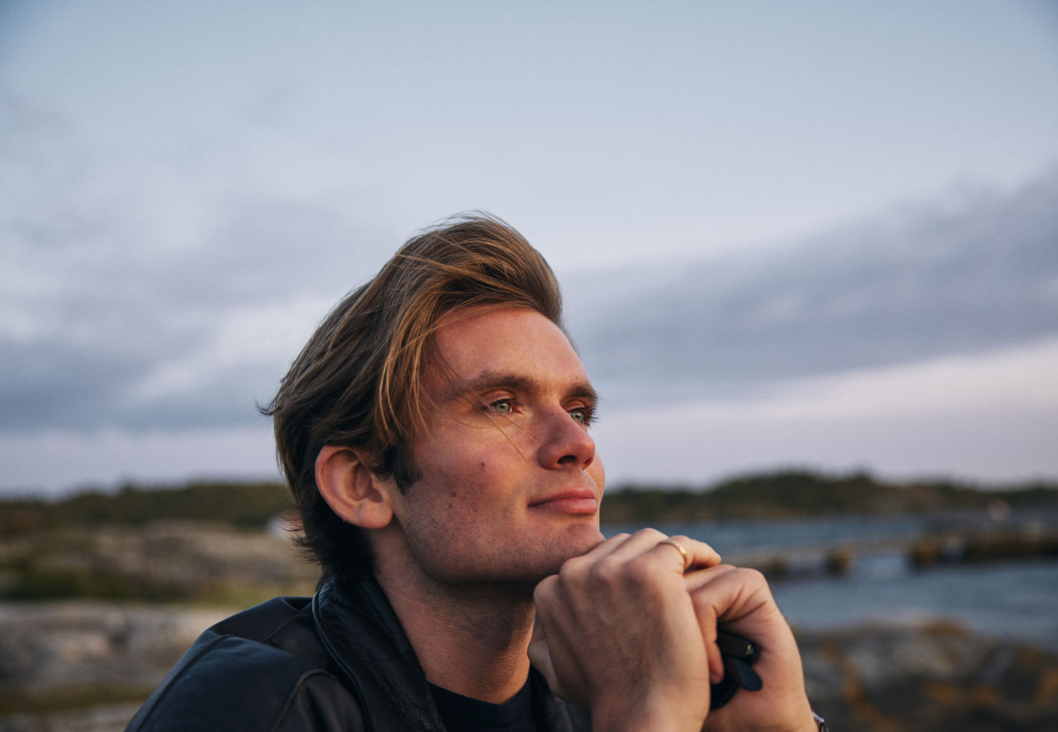 Fridfull bild på en man som sitter och småler utomhus vid vattnet