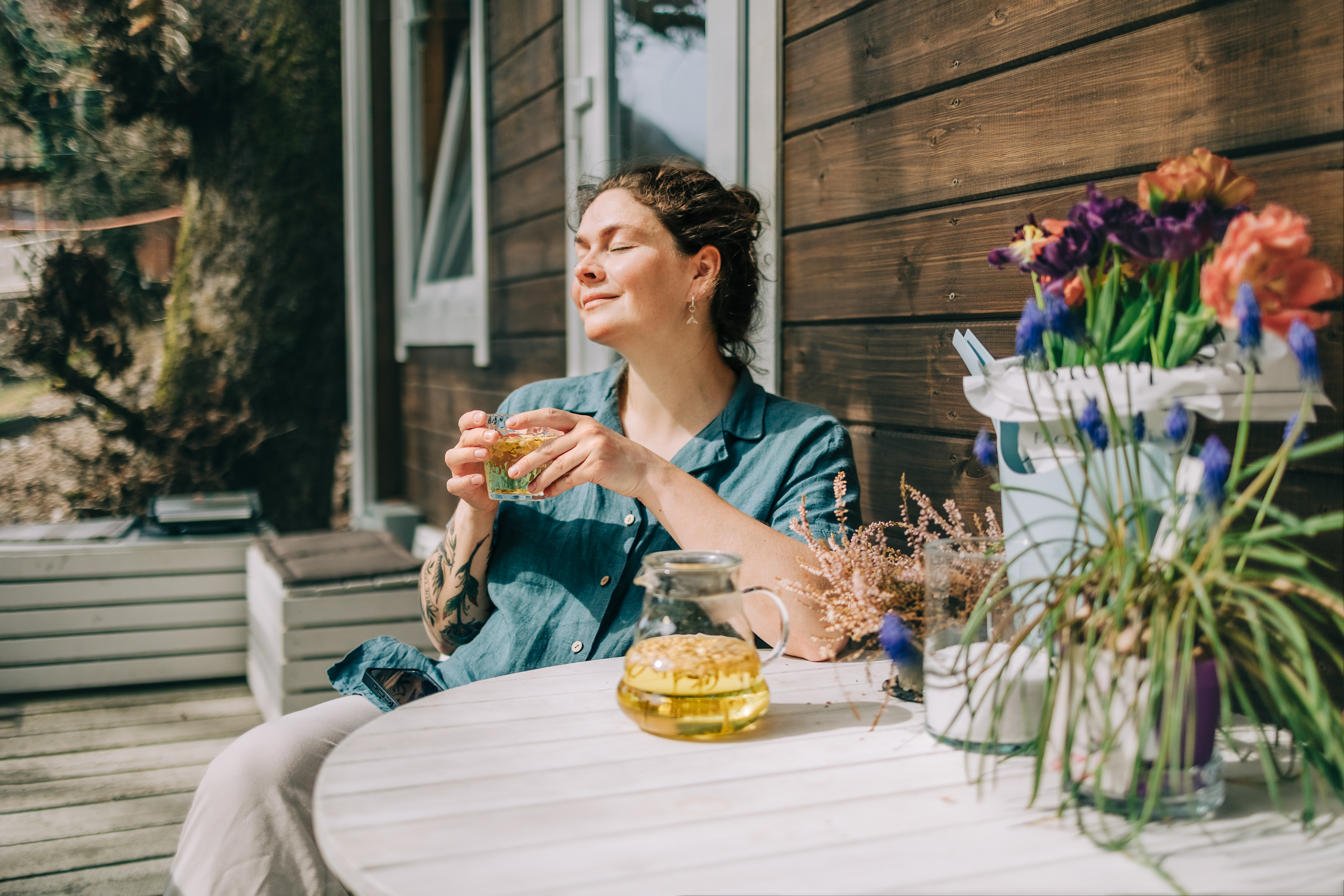 Kvinna sitter på en veranda och njuter av solen med ett glas te