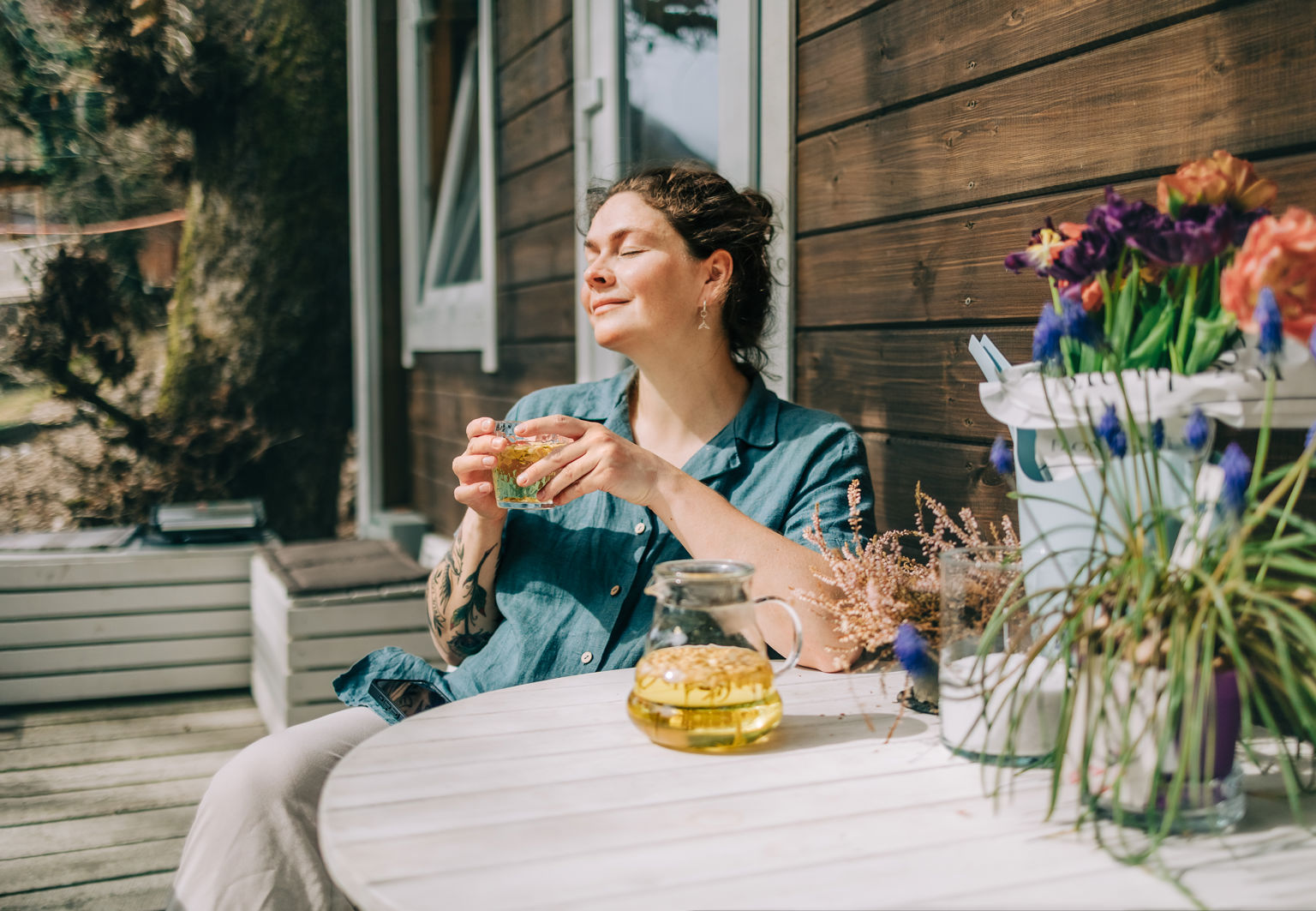 Kvinna sitter på en veranda och njuter av solen med ett glas te