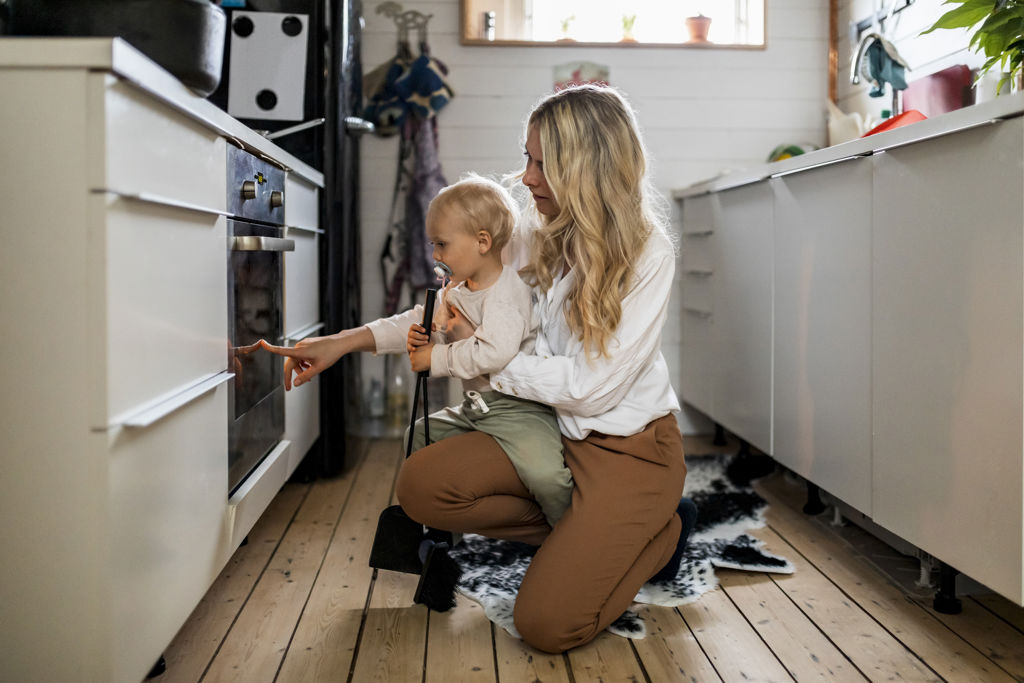 Kvinna och barn sitter på golvet i ett modernt kök och pekar på ugnen