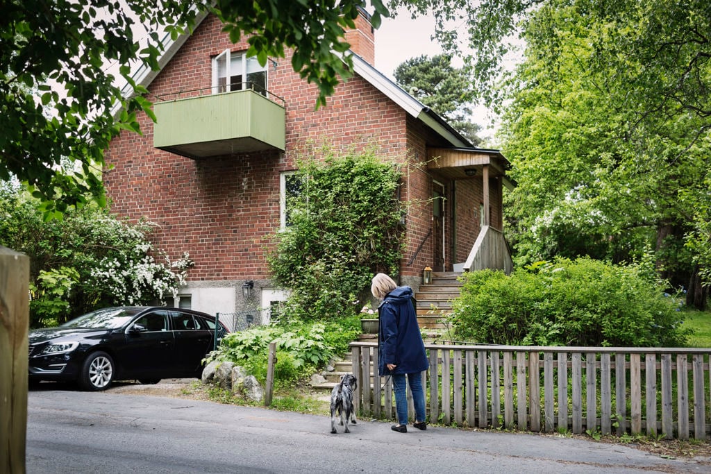 Kvinna med hund står utanför en tegelvilla