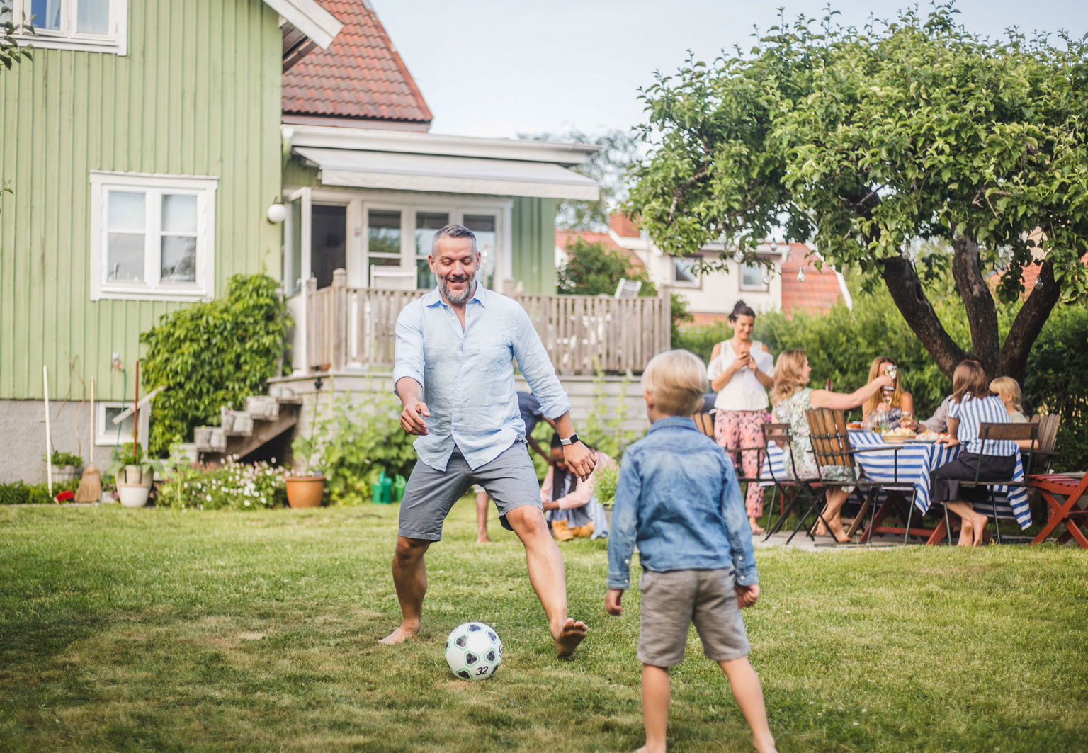 man och pojke spelar fotboll utanför villa