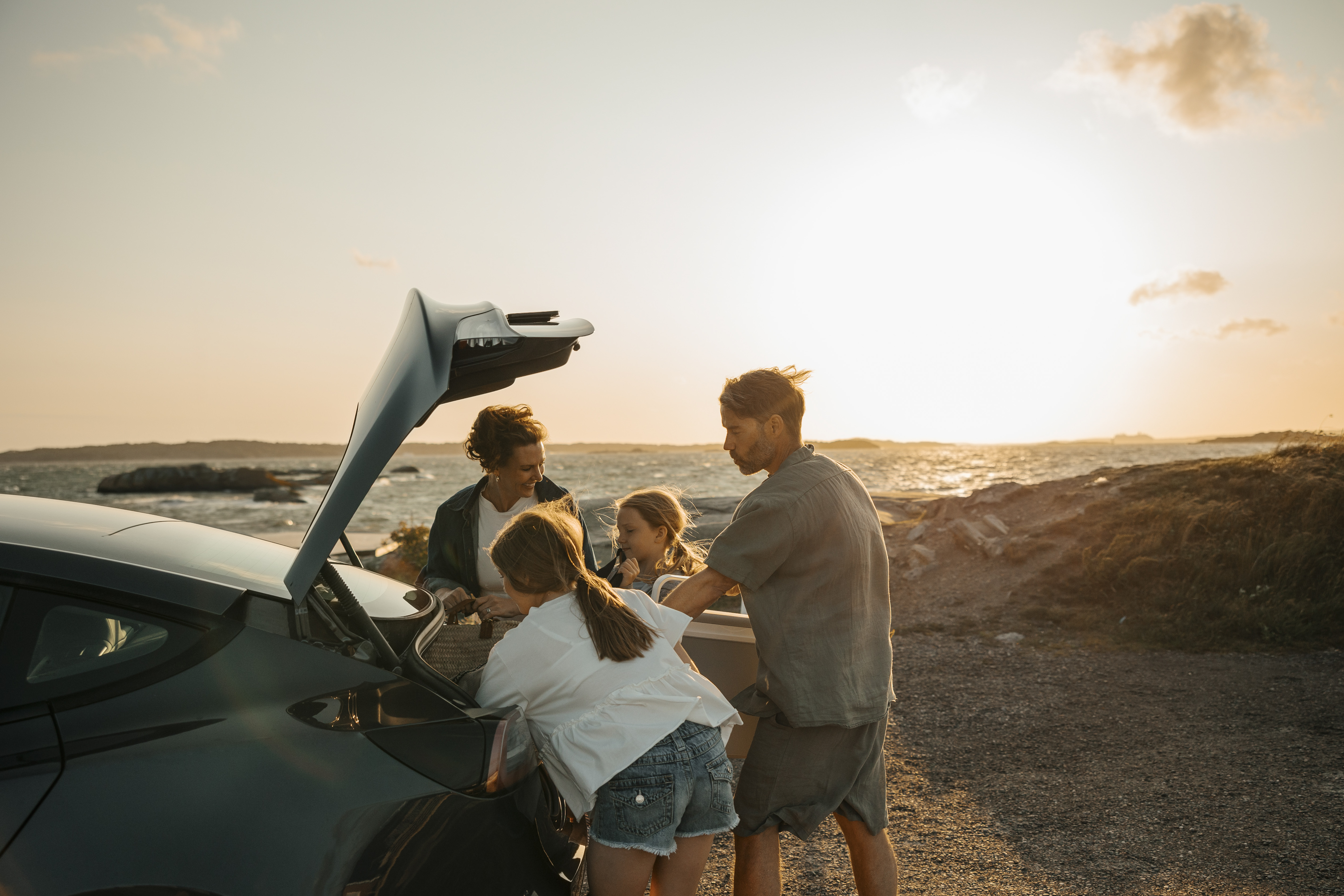 Familj med två barn öppnar bagageluckan på bilen på en blåsig utsiktsplats vid havet