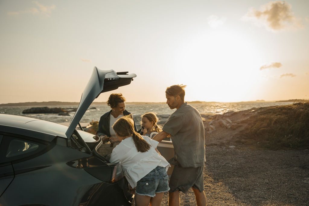 Familj med två barn öppnar bagageluckan på bilen på en blåsig utsiktsplats vid havet
