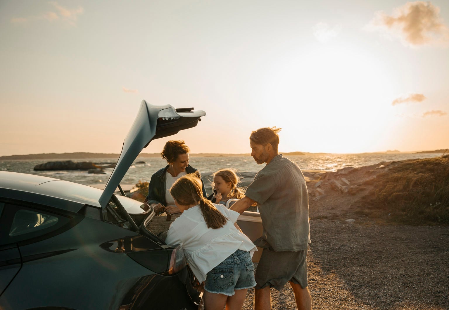 Familj med två barn öppnar bagageluckan på bilen på en blåsig utsiktsplats vid havet