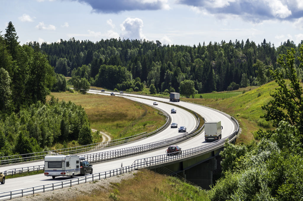 Husbilar, bilar och lastbilar åker på en motorväg i ett sommarlandskap i Sverige