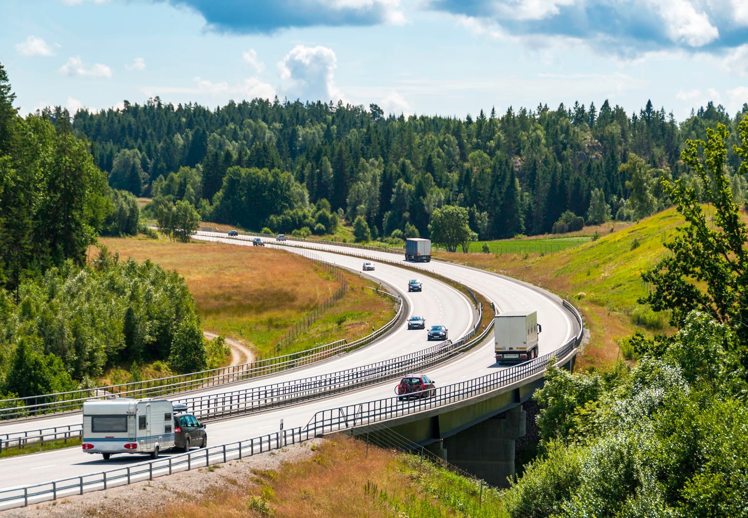 Husbilar, bilar och lastbilar åker på en motorväg i ett sommarlandskap i Sverige