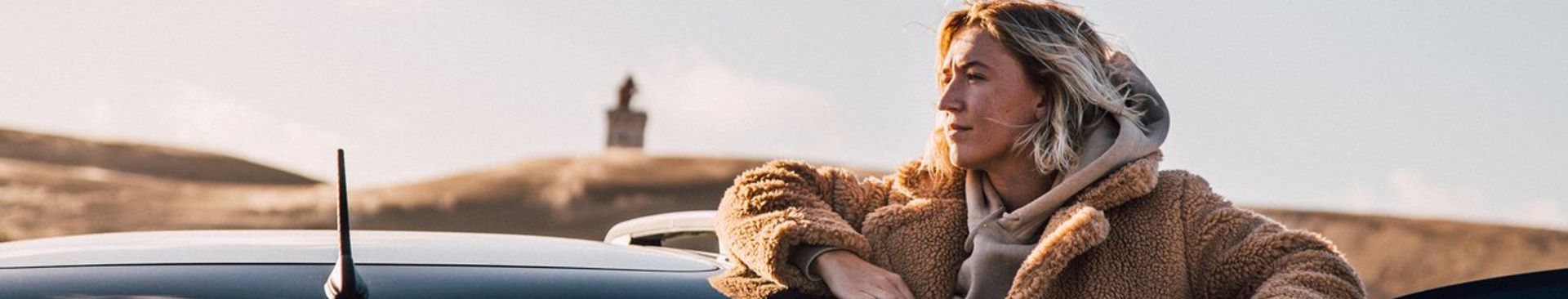 Kvinna står vid en öppen bildörr på ett stort fält