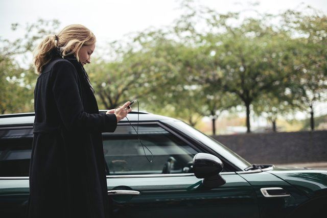 Kvinna tittar på sin telefon bredvid sin parkerade bil