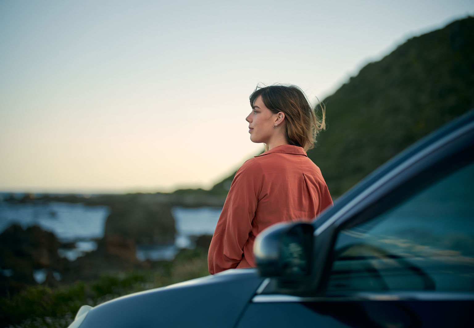 Kvinna står framför sin bil och tittar på utsikt över havet