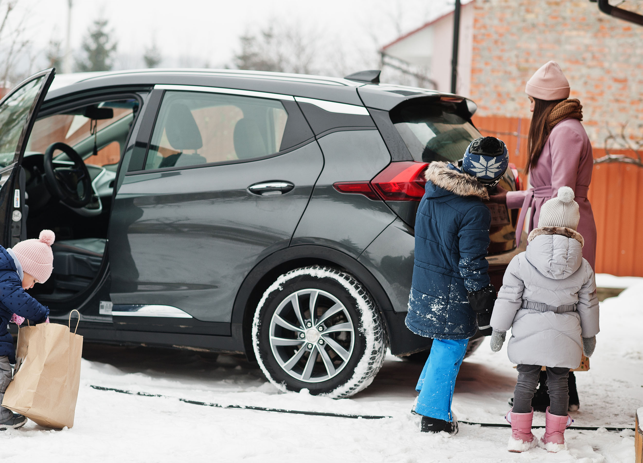 kvinna med tre barn står vid en parkerad bil