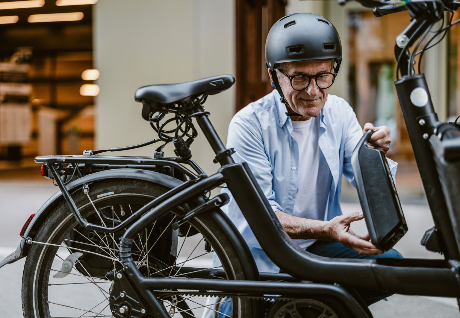 Äldre man med hjälm håller i elcykelns batteri på gatan