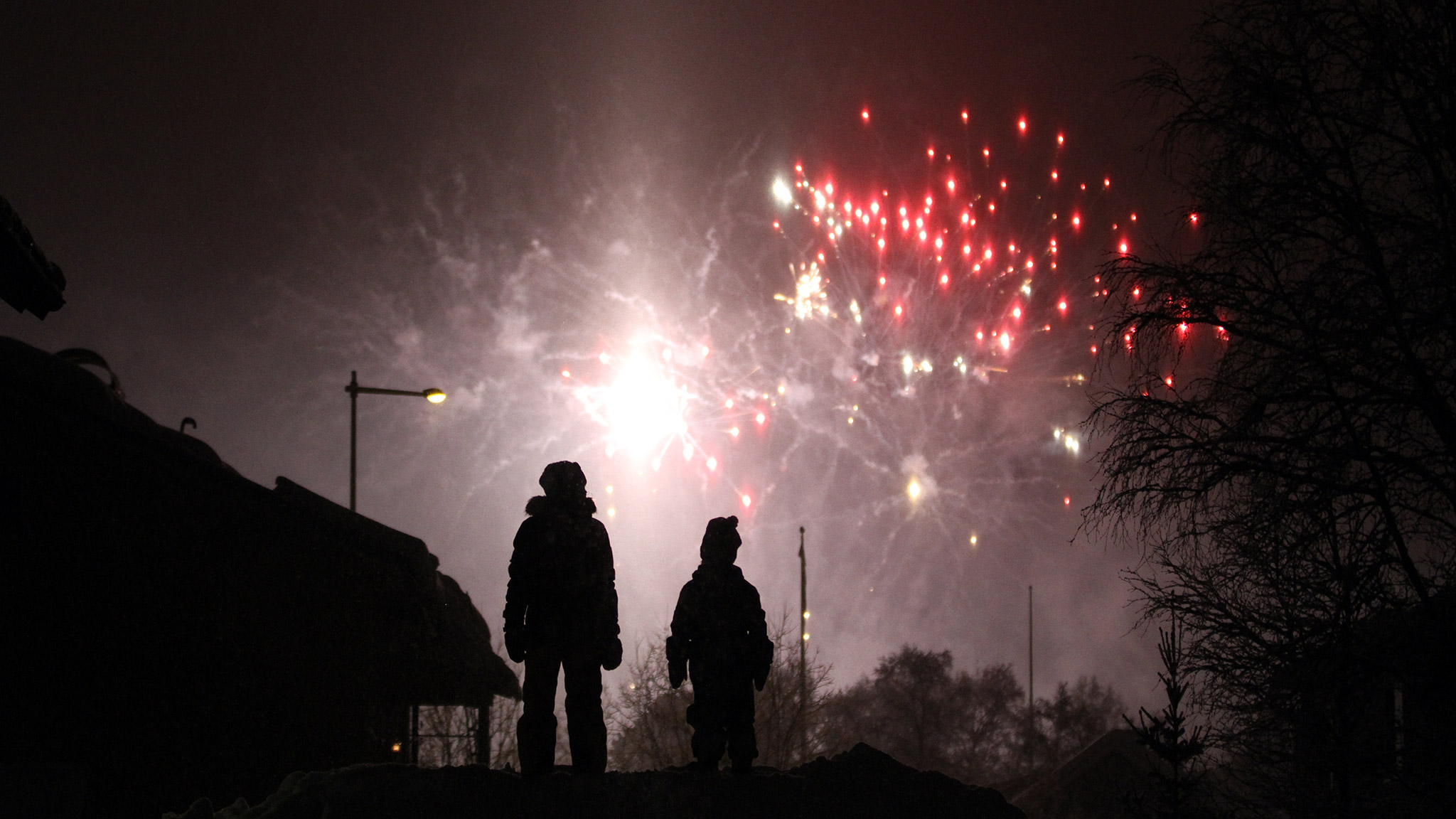 Barn är ute på kvällen och tittar upp på fyrverkerier