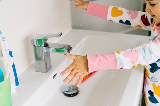 Flicka tvättar händerna i ett handfat