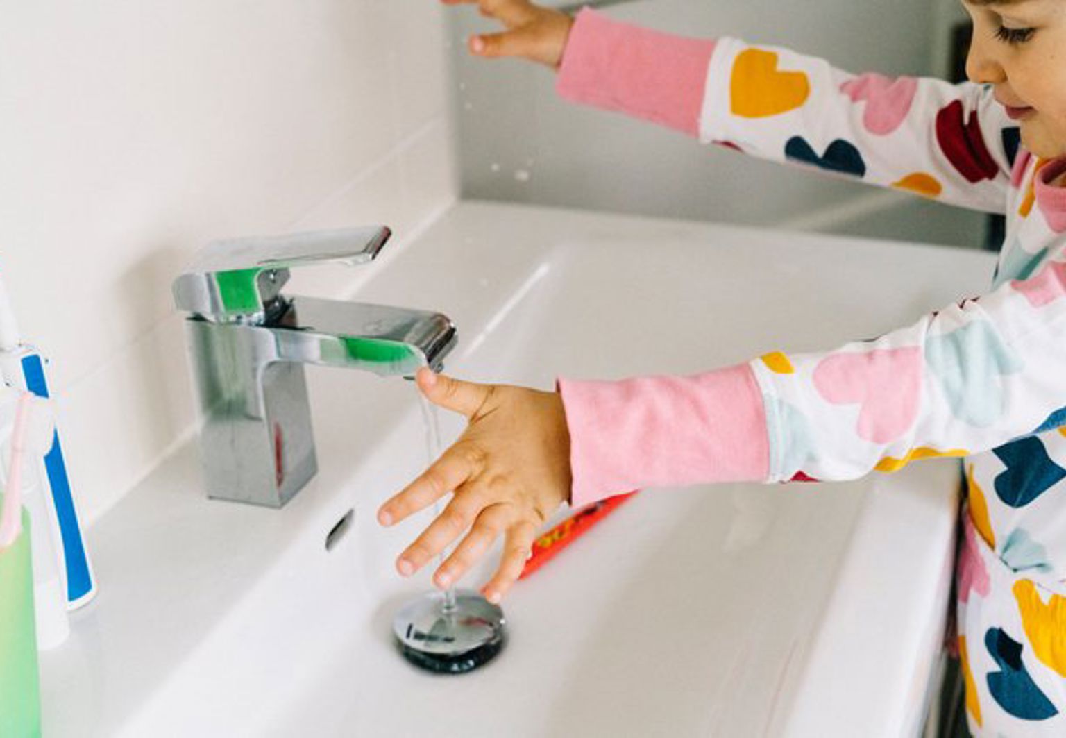 Flicka tvättar händerna i ett handfat