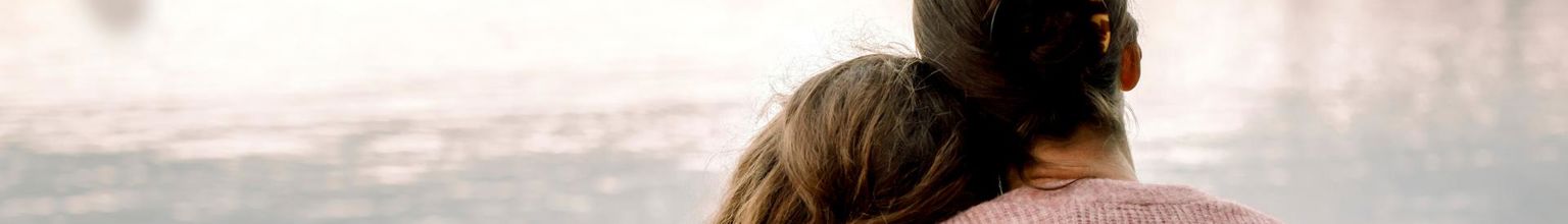 mamma håller om sin dotter vid en sjö