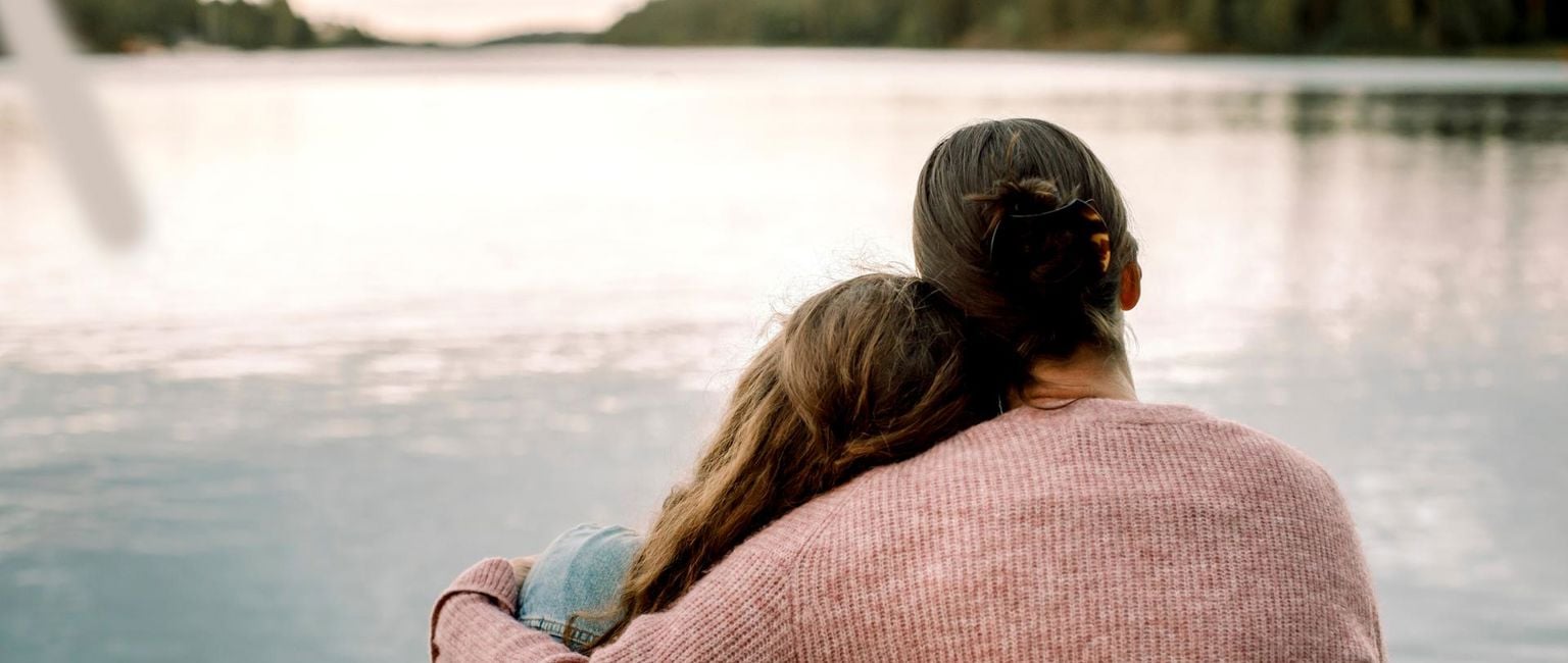 mamma håller om sin dotter vid en sjö