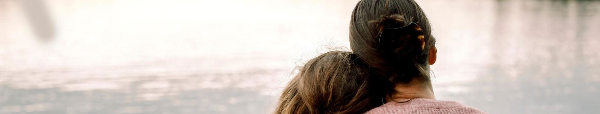 mamma håller om sin dotter vid en sjö