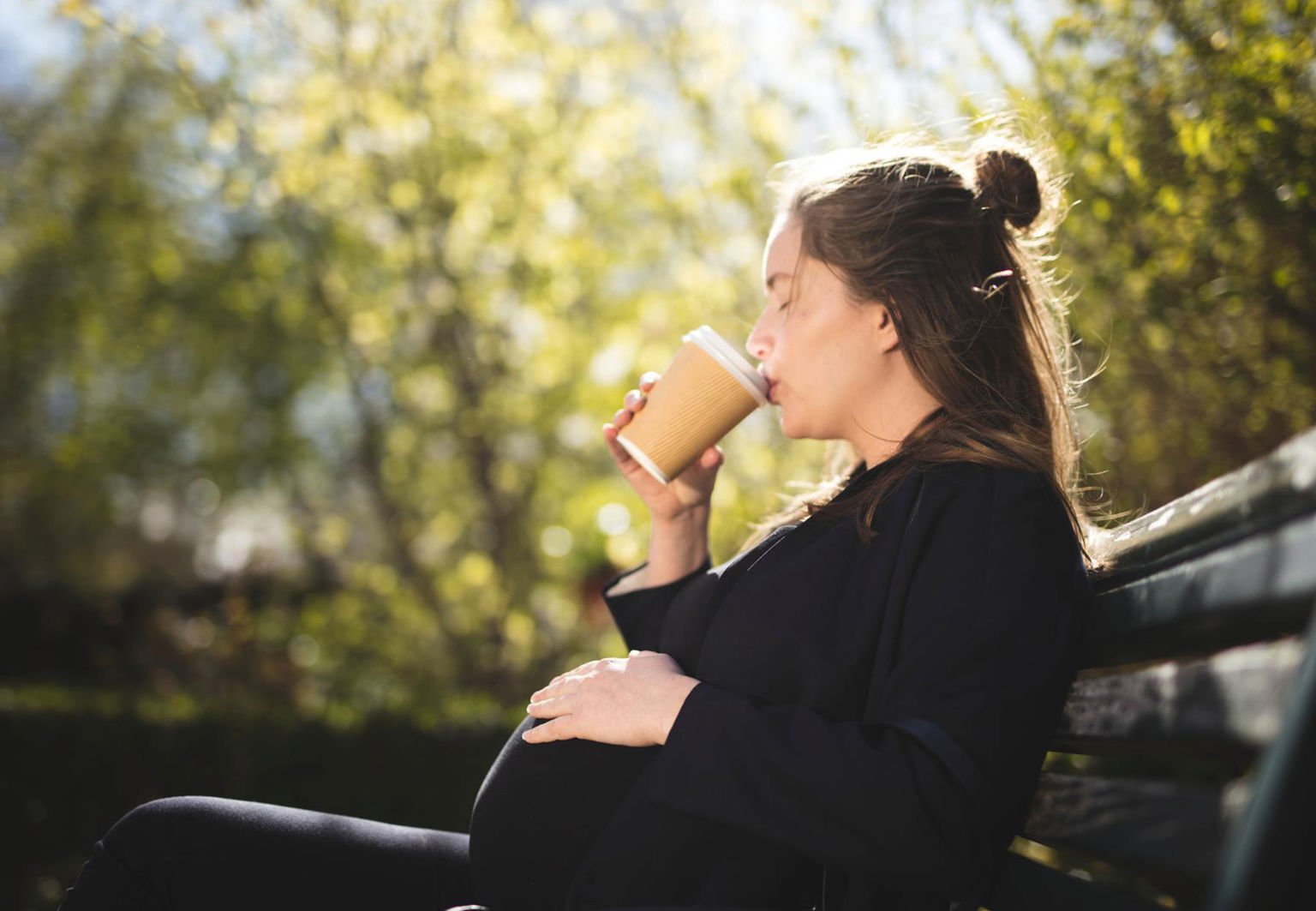 ung kvinna gravid på en parkbänk i solen