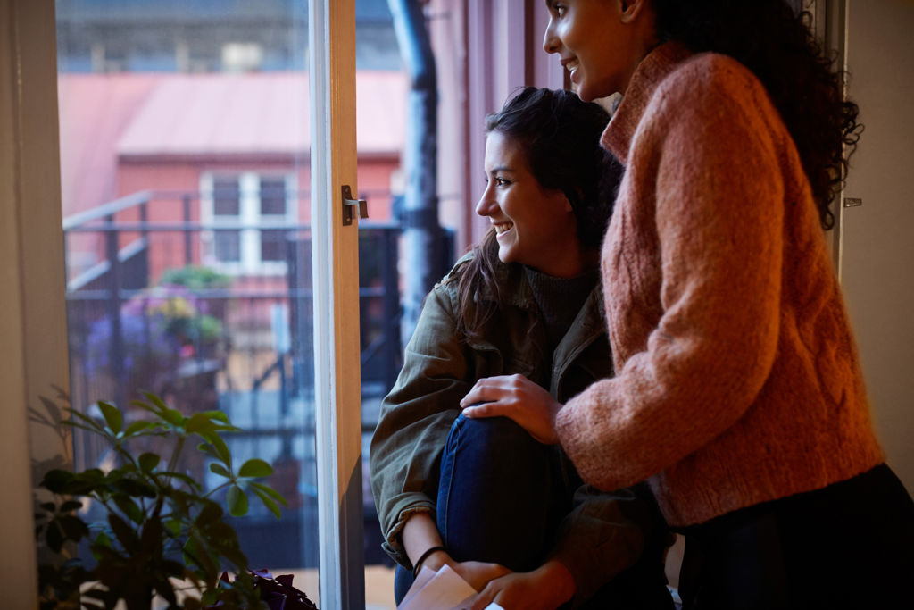 Två kvinnor i en lägenhet som tittar ut genom ett fönster