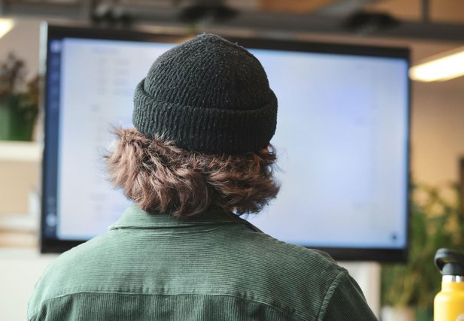 Man med mössa arbetar på stor skärm