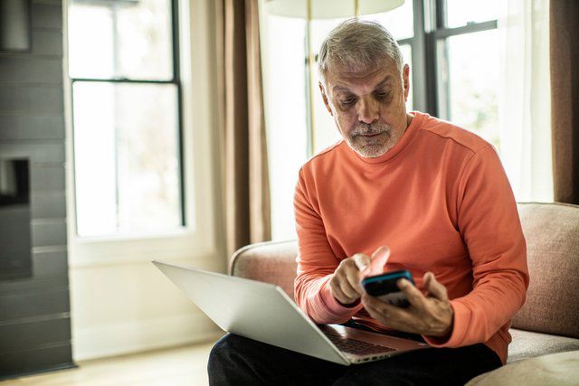 Äldre man sitter framför laptop med sin telefon i handen