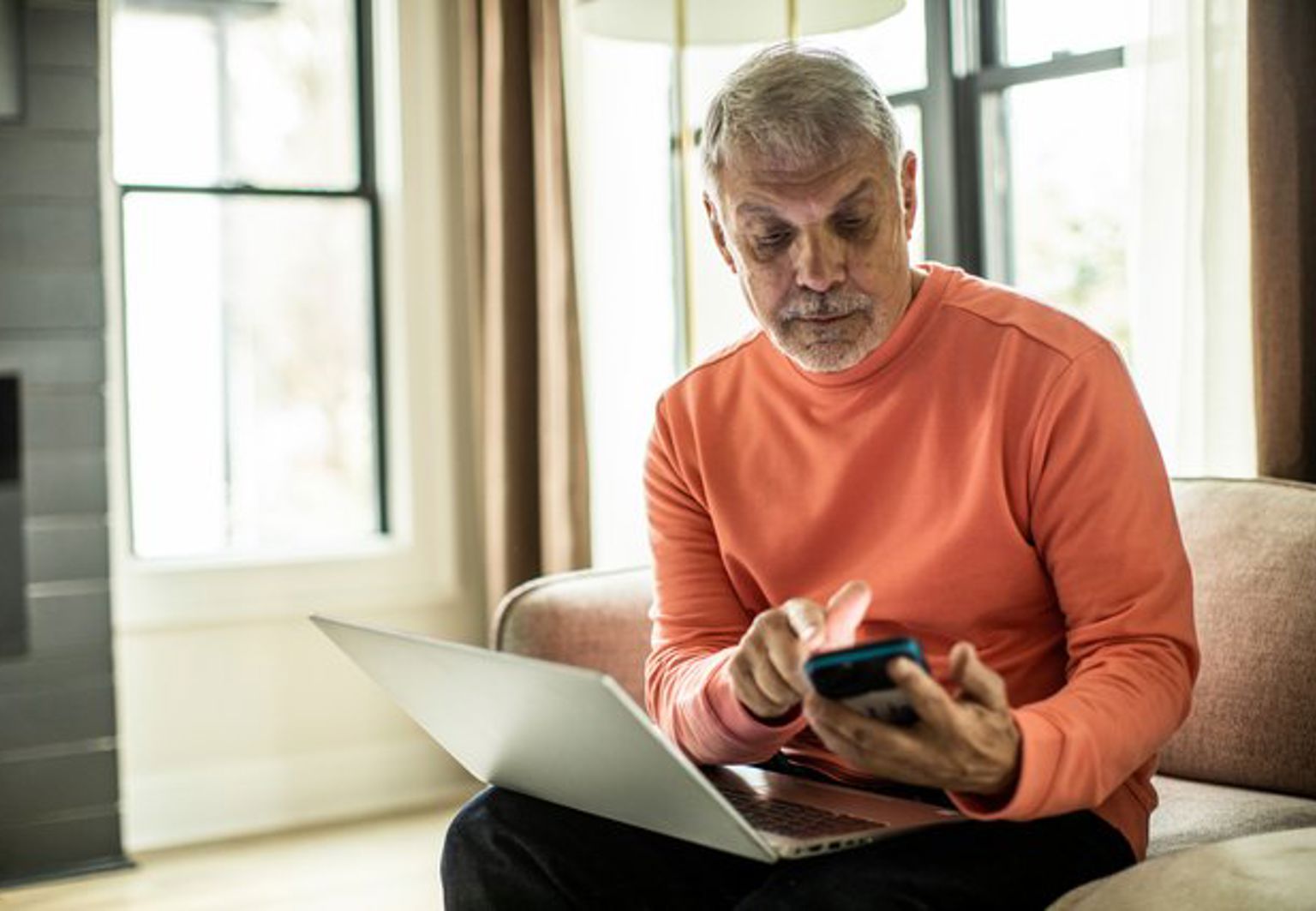 Äldre man sitter framför laptop med sin telefon i handen