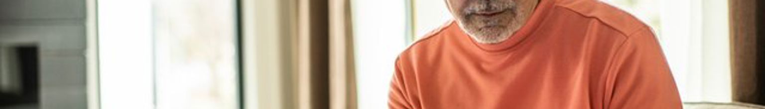 Äldre man sitter framför laptop med sin telefon i handen